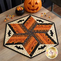 a table with a pumpkin on it and a quilted star in the center, surrounded by candy