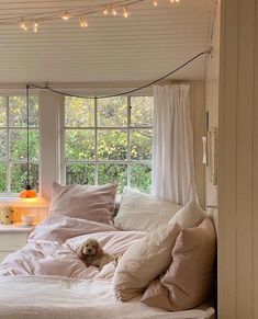 a bed with white sheets and pillows in front of a window filled with fairy lights