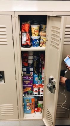 a man holding a smart phone next to a metal locker filled with food and drinks