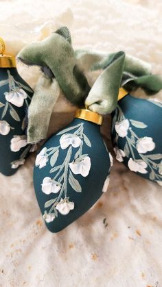 three blue ornaments with white flowers and green ribbon on them sitting on a bed sheet