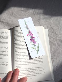 a person holding an open book with flowers on it and a piece of paper sticking out of the book