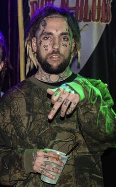 a man with tattoos and piercings on his face holding a drink in front of him