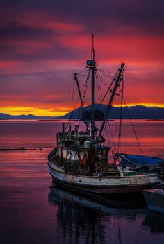 a boat sitting on top of a body of water under a colorful sky with mountains in the background