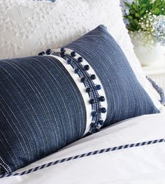 a blue and white pillow with tassels on the edges sitting on a bed