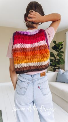 a woman wearing a multicolored knitted vest and jeans, with her hands on her head