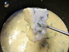 a ladle full of cheese sauce being held by a spoon in a skillet