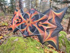 an artistically designed umbrella sitting on top of a moss covered rock in the woods