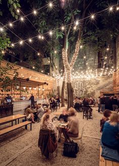 people are sitting at tables in the middle of an outdoor area with lights strung overhead