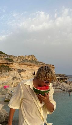 a man holding a piece of watermelon near the ocean