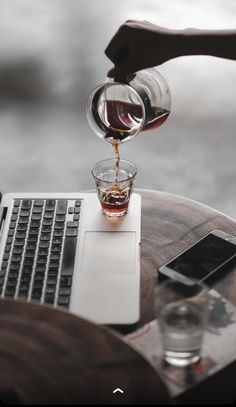 someone pouring tea into a glass on top of a laptop