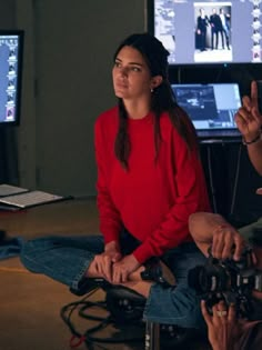 a woman sitting on the floor in front of two monitors and holding a video camera