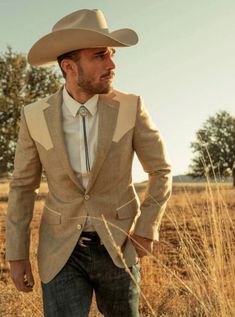 a man in a suit and cowboy hat standing in the middle of an open field