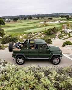 a green jeep driving down a road next to a golf course