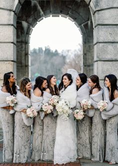 a group of women standing next to each other in front of a stone arch holding bouquets