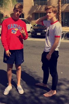 two young men standing in the middle of a street talking to each other with palm trees behind them