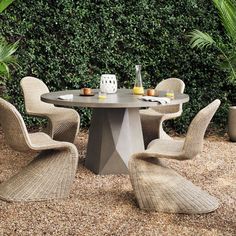 an outdoor table with four chairs around it in front of some bushes and plants on the ground