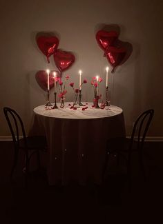 a table topped with lots of red heart shaped balloons next to two black chairs and a white table cloth