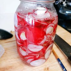 a glass jar filled with liquid sitting on top of a wooden table next to utensils