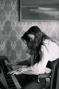 a woman sitting at a piano in front of a wall with a painting on it