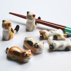 small ceramic cats sitting on top of a table next to a green pen and pencil