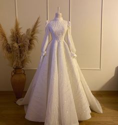 a white wedding dress sitting on top of a wooden floor next to a vase filled with dry grass