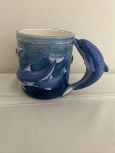 a blue and white coffee mug with dolphins on it's side sitting on a table