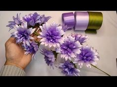 purple flowers are being held by someone's hand near some spools of thread