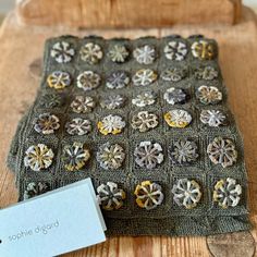 a wooden table topped with a green knitted cushion covered in small decorative buttons and a white tag