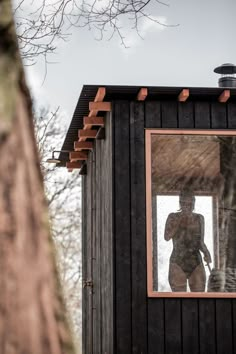 a person standing in the window of a small building with a mirror on it's side