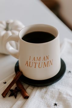 a cup of coffee sitting on top of a table next to cinnamon sticks and an orange pumpkin