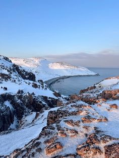 the snow covered mountains are next to the water and some rocks in the foreground