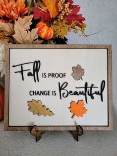 a sign that says fall is proof change is beautiful with leaves and acorns