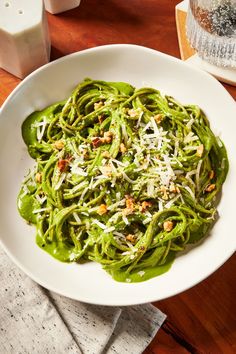 a white bowl filled with green pasta on top of a wooden table next to a napkin