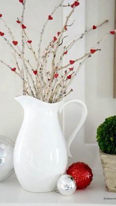 a white vase filled with branches and red berries on top of a table next to ornaments