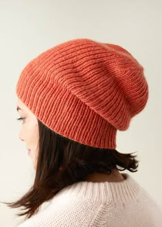 a woman wearing an orange knitted beanie, looking down at her head and back