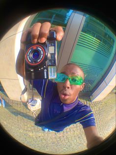 a man wearing sunglasses taking a selfie in front of a building with a camera