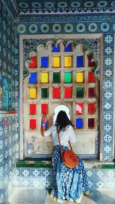 a woman sitting on the ground in front of a wall with colorful glass blocks behind her