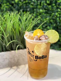 an iced drink with lime and orange slices on the rim, sitting on a table in front of some bushes