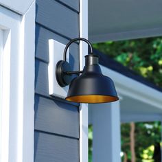 an outdoor wall light on the side of a blue house with trees in the background