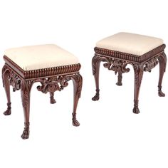 two wooden stools with white upholstered cushions on each side and an intricately carved design