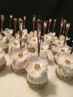 there are many cupcakes with white flowers on them and gold stems sticking out of the top