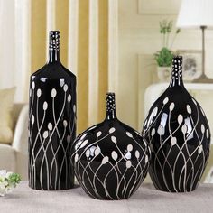 three black vases sitting on top of a table in front of a white couch