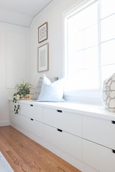 a room with white walls and wooden flooring is pictured in this image, the window seat has two pillows on it