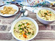 two white bowls filled with soup and crackers on top of a brick wall next to a spoon