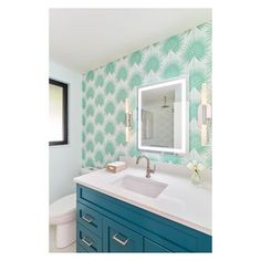 a bathroom with green and white wallpaper, blue vanity cabinets and a large mirror