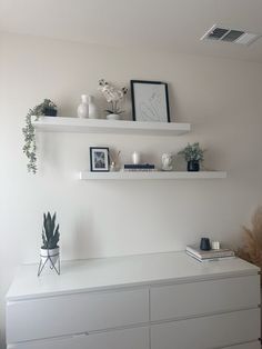 two white shelves with plants and pictures on them