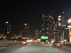 the city skyline is lit up at night, with cars driving down the street in front of them