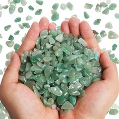 two hands holding green and white rocks on top of each other in front of scattered stones