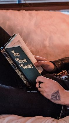 a person sitting on a couch with a book in their hand and tattoos on their arm