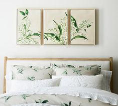 two paintings on the wall above a bed with white linens and green plants in them